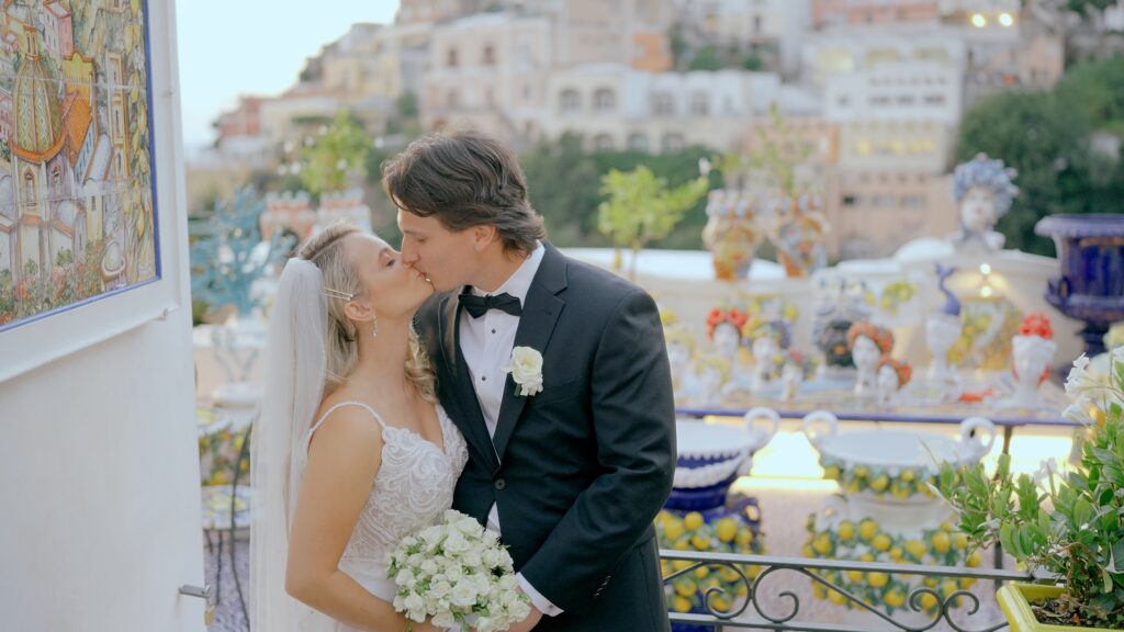 Bride and groom kissing on a Positano terrace with colorful ceramics, lemon decorations and Amalfi Coast views.