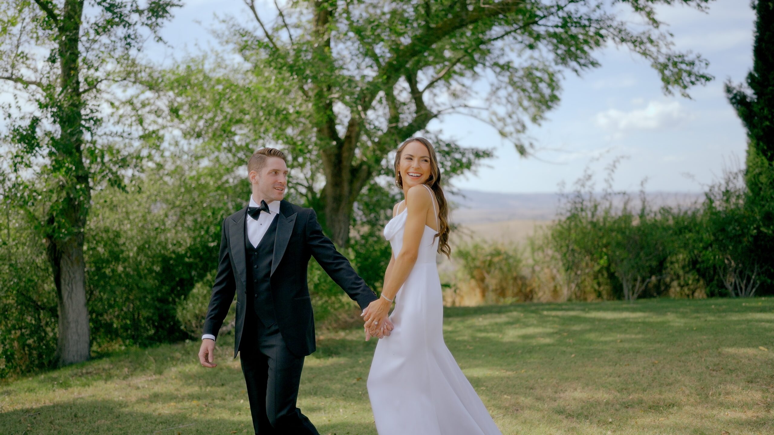 Bride and groom holding hands and walking through a green outdoor garden on their wedding day.
