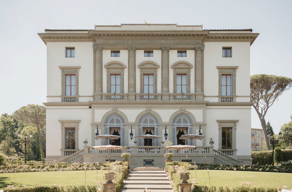 Large neoclassical villa with tall columns, arched windows, formal gardens, stone pathway, and manicured lawns in front.