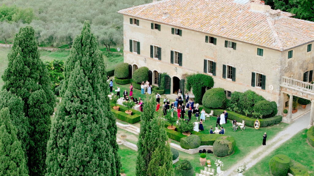 Why U.S. Couples Choose Italian Wedding Videographers 2 Aerial view of a luxury wedding reception at a historic Tuscan villa surrounded by cypress trees and gardens in Italy.