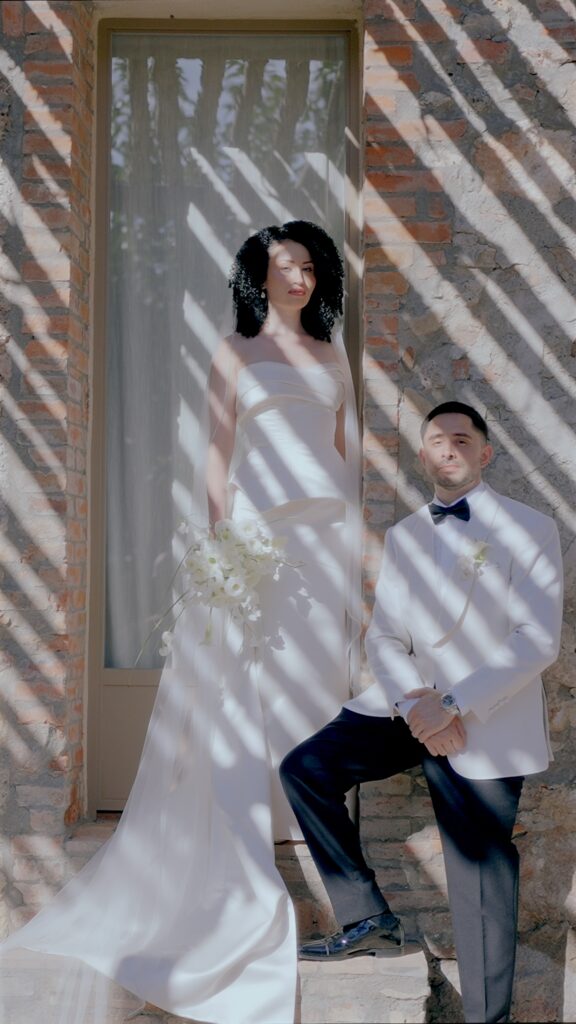 Elegant bride and groom portrait at La Pescaia Resort in Tuscany with dramatic sunlight, rustic stone architecture and modern wedding fashion.