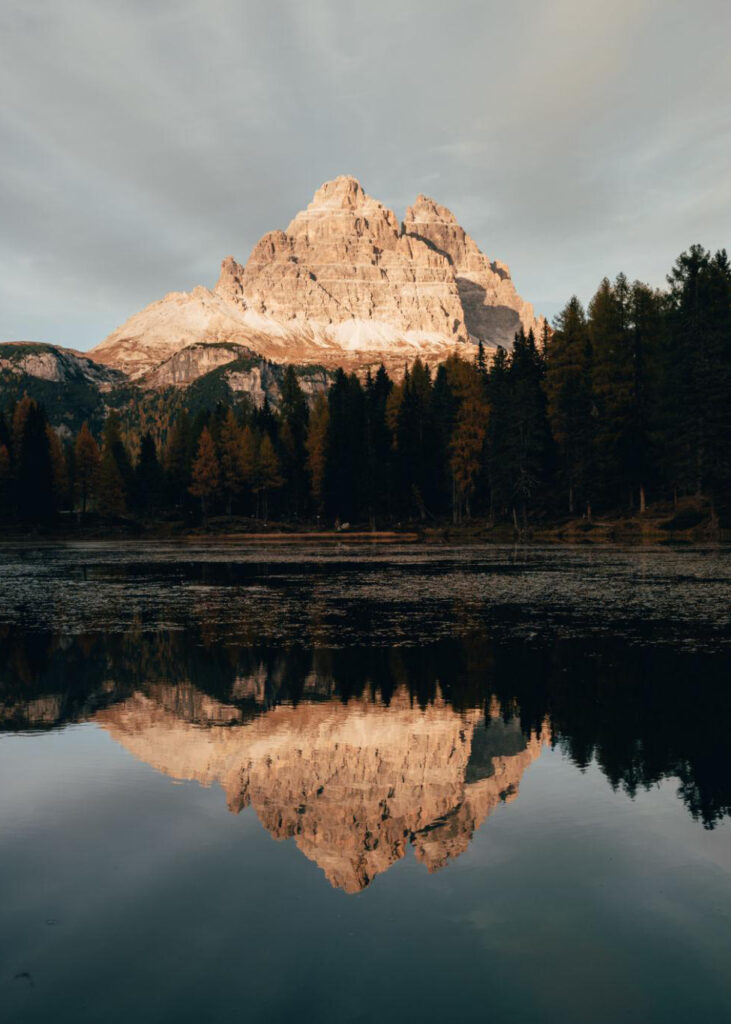 Cinematic sunset over a mountain lake in the Dolomites surrounded by pine forests and dramatic alpine peaks.