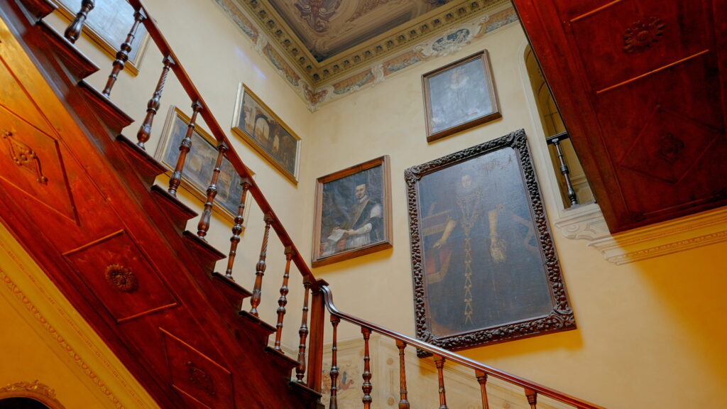 Why U.S. Couples Choose Italian Wedding Videographers 6 Low-angle view of a grand wooden staircase in an Italian villa, decorated with historic oil portraits and original frescoed ceilings.