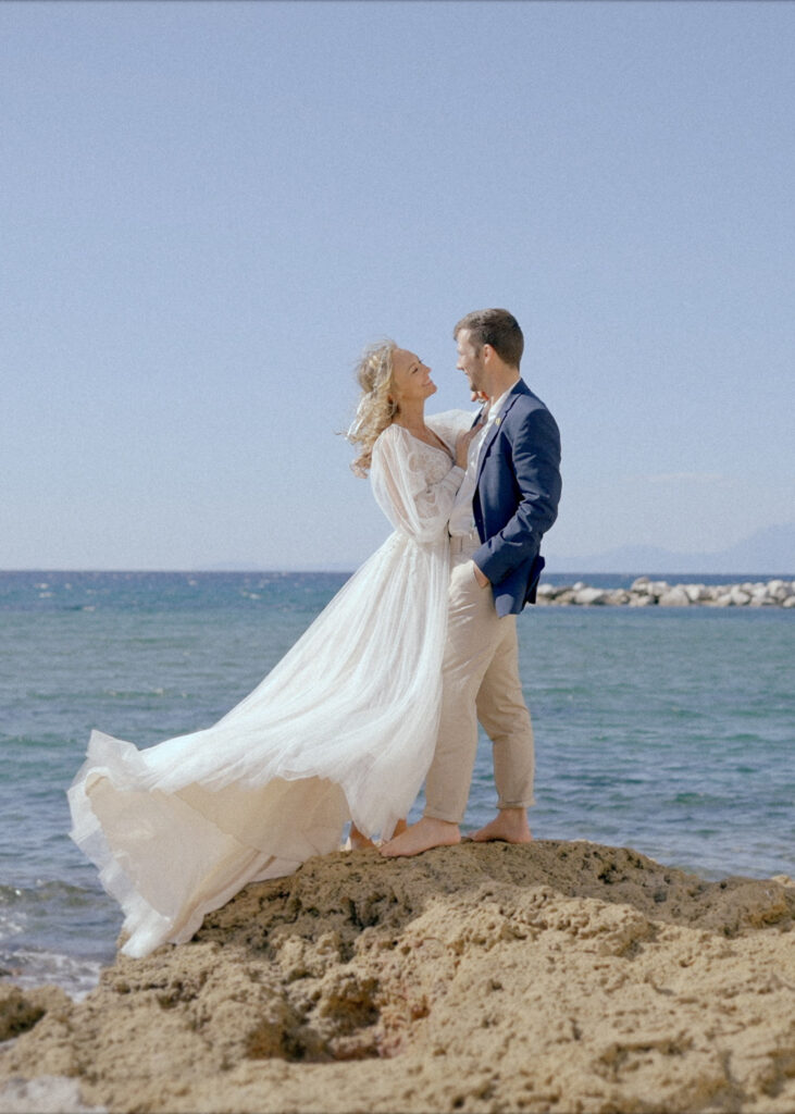Couple embracing on the seaside rocks during a romantic Italian elopement by the Mediterranean coast.