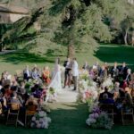 Luxury outdoor wedding ceremony at La Pescaia Resort in Tuscany with floral decorations, seated guests and elegant garden setting.