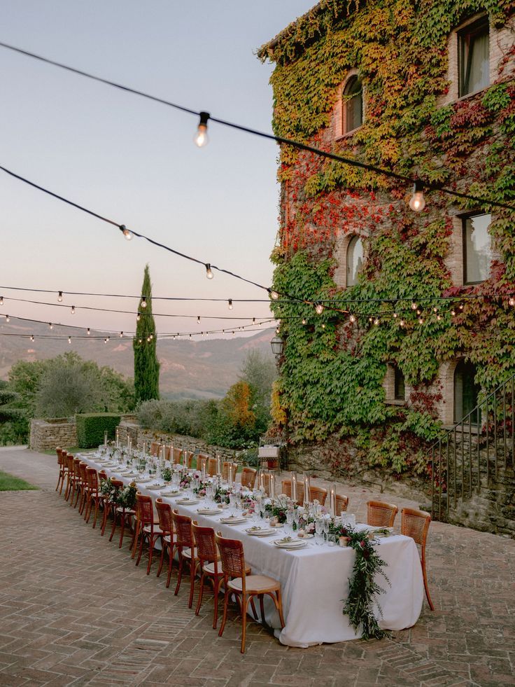Luxury outdoor wedding reception in Umbria, Italy, with long imperial table, string lights, and ivy-covered historic villa.