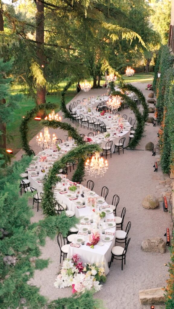 Elegant outdoor wedding reception at La Pescaia Resort in Tuscany with long imperial tables, chandeliers, candlelight and floral arches surrounded by the Italian countryside.