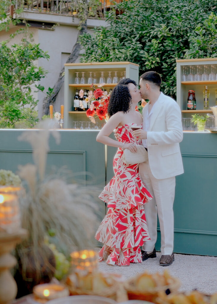 Elegant couple kissing at a luxury wedding cocktail hour in Tuscany with stylish fashion, outdoor bar setup and romantic Italian atmosphere.