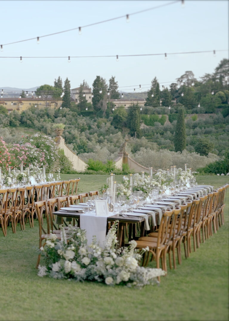 Destination Wedding Videographer Italy 3 Luxury outdoor wedding reception in Tuscany with imperial tables, white floral arrangements, string lights and Italian countryside views.