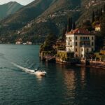 Luxury villa overlooking Lake Como with a small boat crossing the water at sunset in Italy