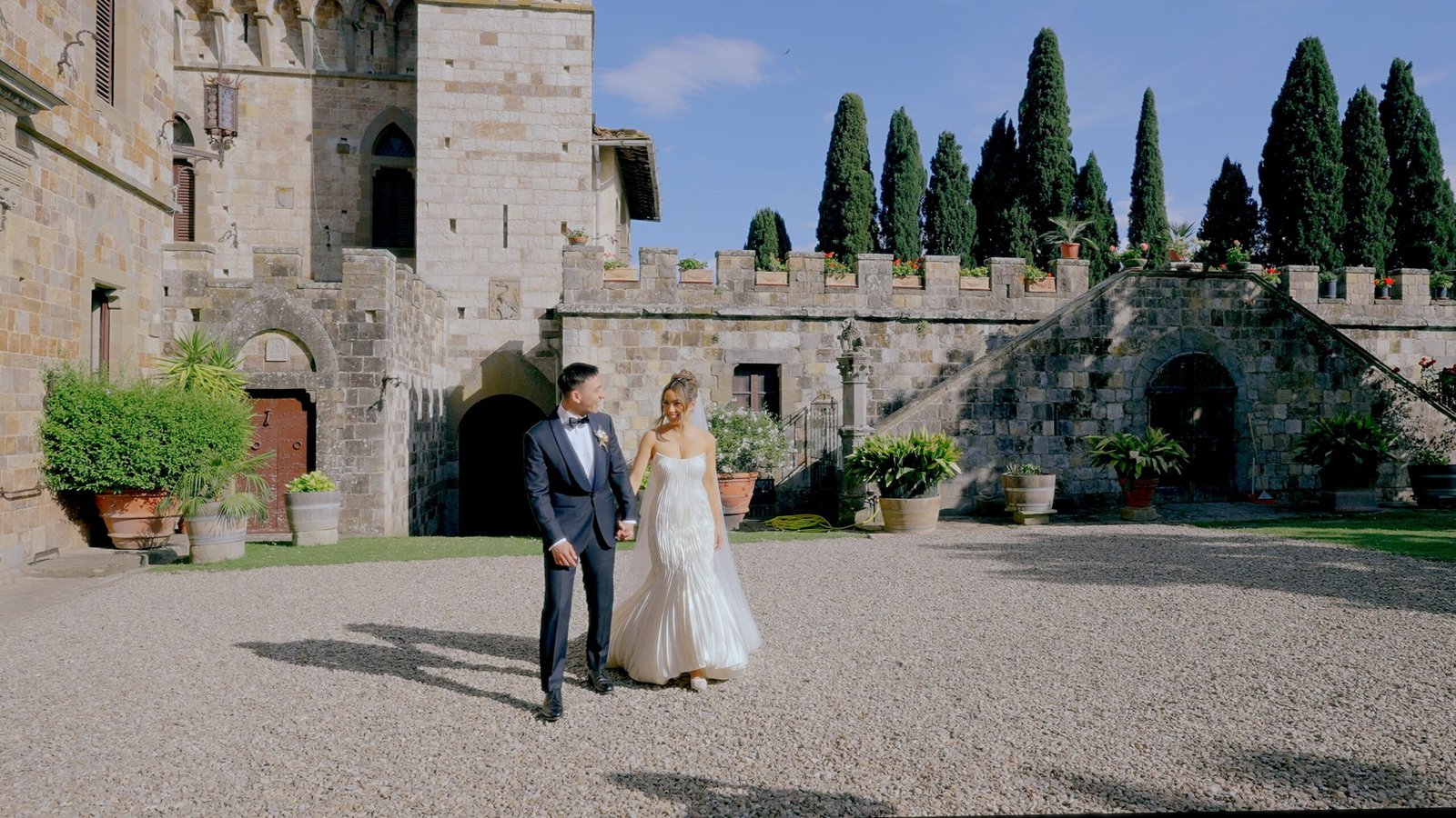 Italian wedding destination in Tuscany — bride and groom in the courtyard of a medieval castle surrounded by cypress trees