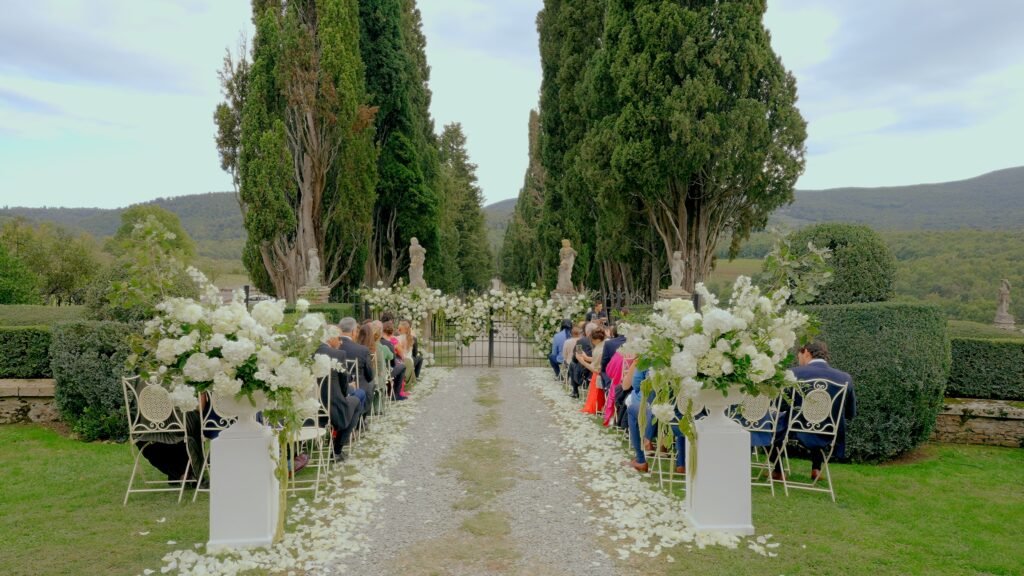 Italian wedding videographer for Los Angeles couples — outdoor wedding ceremony in Tuscany surrounded by cypress trees, white flowers and rolling hills