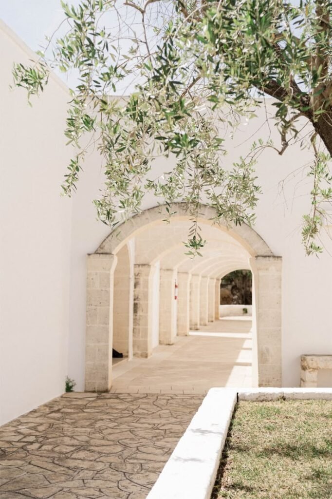 Wedding Videographer Puglia 1 Whitewashed stone arches and an overhanging olive tree in a Puglia masseria courtyard